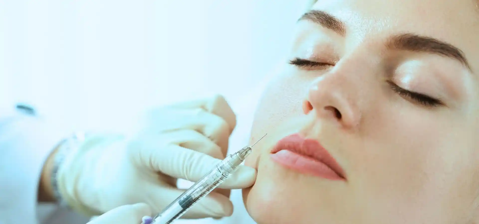 Close-up of a cosmetic facial injection procedure, with a healthcare professional wearing gloves administering an injectable treatment to a woman’s lower face in a clinical setting.