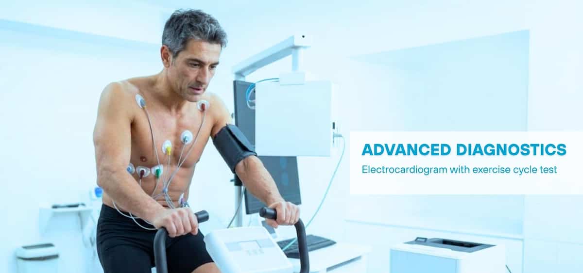 A man performing an exercise stress test on a stationary bike while connected to ECG sensors, representing advanced diagnostics in a clinical environment.