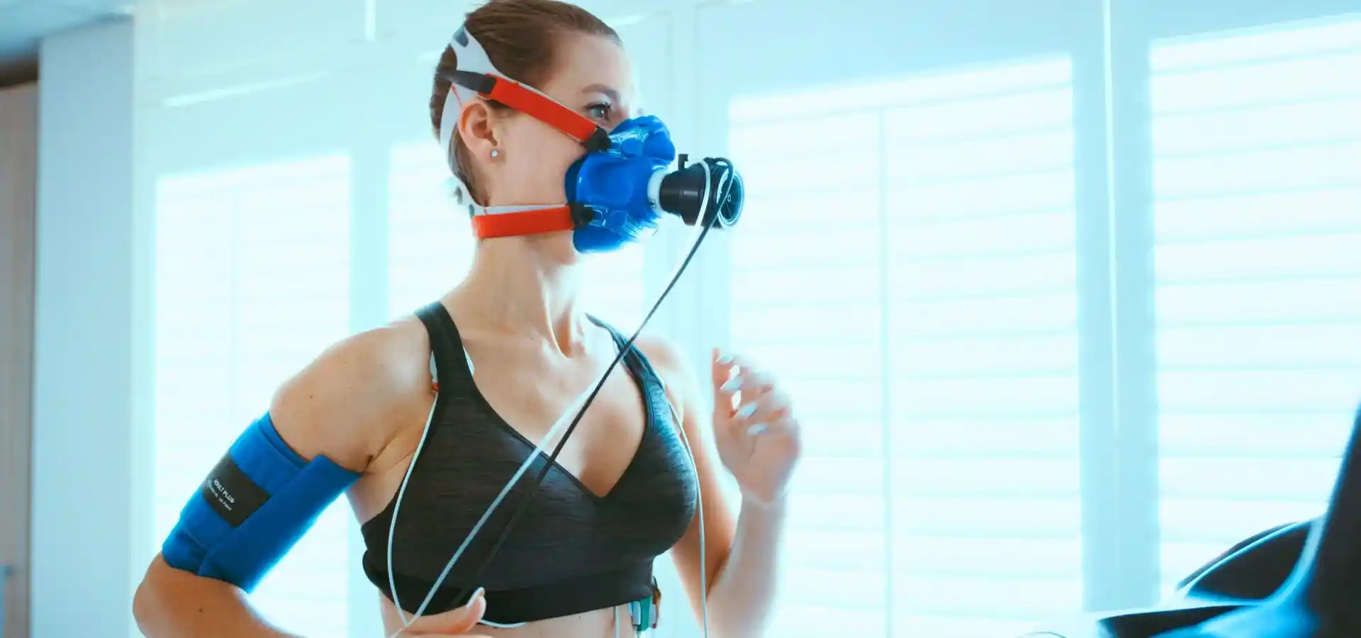 A woman undergoes a VO₂ max fitness assessment while running on a treadmill wearing a respiratory testing mask.