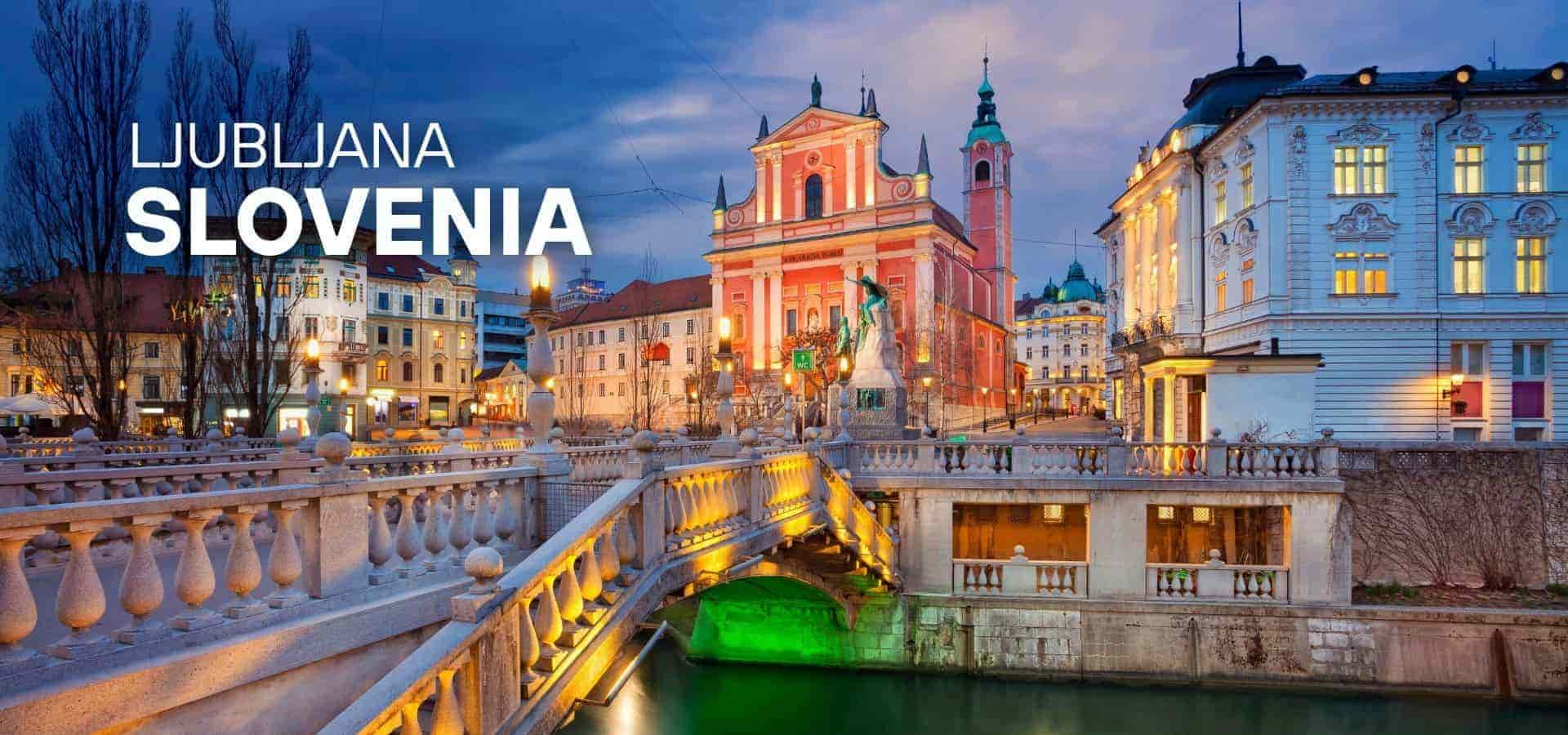 Evening view of Ljubljana, Slovenia with a lit historic bridge, colorful buildings, and a canal reflecting city lights