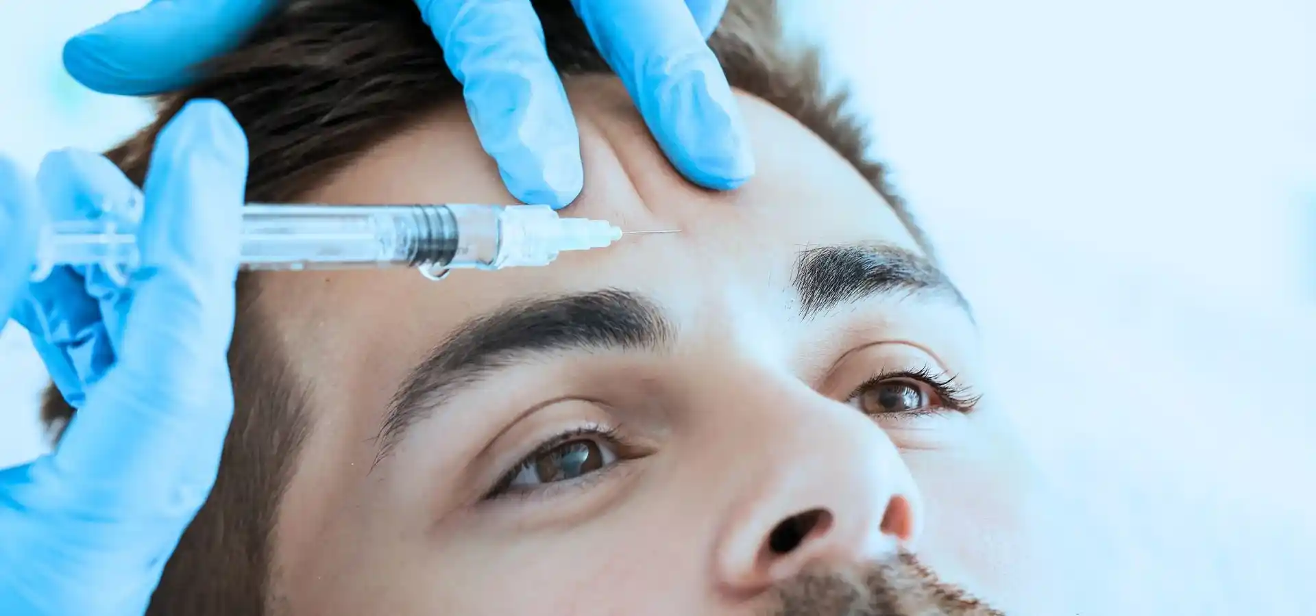 Close-up of a cosmetic forehead injection procedure, with a healthcare professional wearing blue gloves administering an injectable treatment to a man's forehead in a medical clinic.