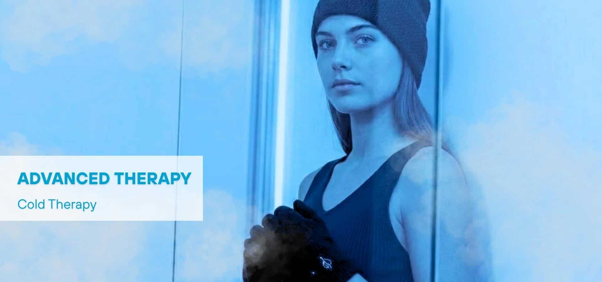 A woman standing inside a cold therapy chamber, wearing a beanie and gloves, surrounded by cool blue light and mist, representing advanced cold therapy treatment.