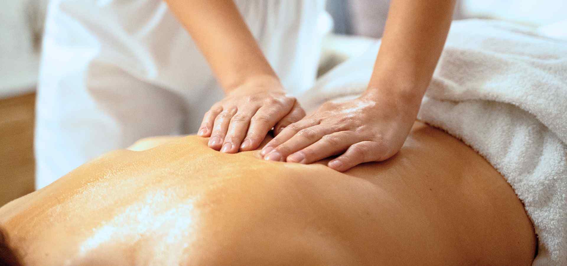 Close-up of a professional spa massage treatment, with a therapist applying gentle pressure to a client’s back using both hands in a relaxing wellness setting.