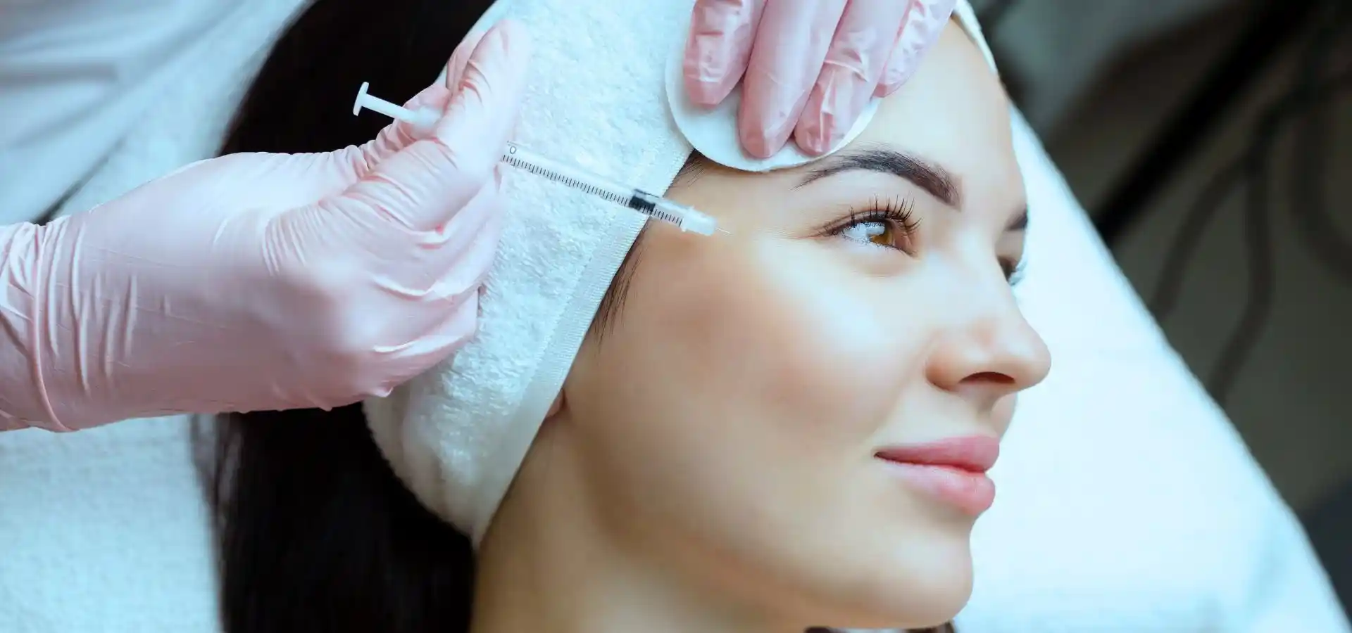 Close-up of a cosmetic injectable treatment, showing a medical professional administering an injection near a woman’s temple during a facial rejuvenation procedure in a clinical setting.