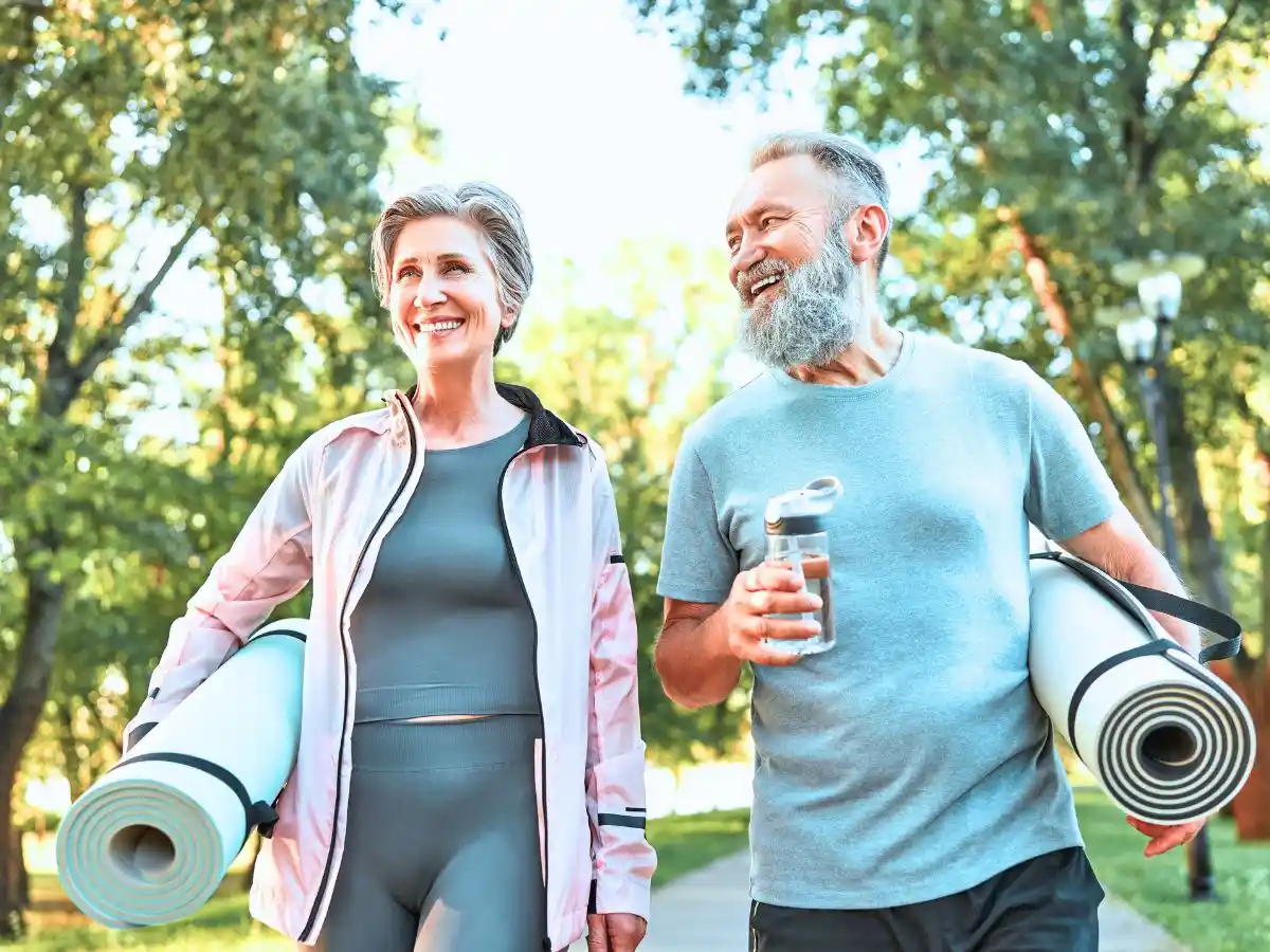 Older couple walking outdoors with yoga mats, promoting an active and healthy lifestyle