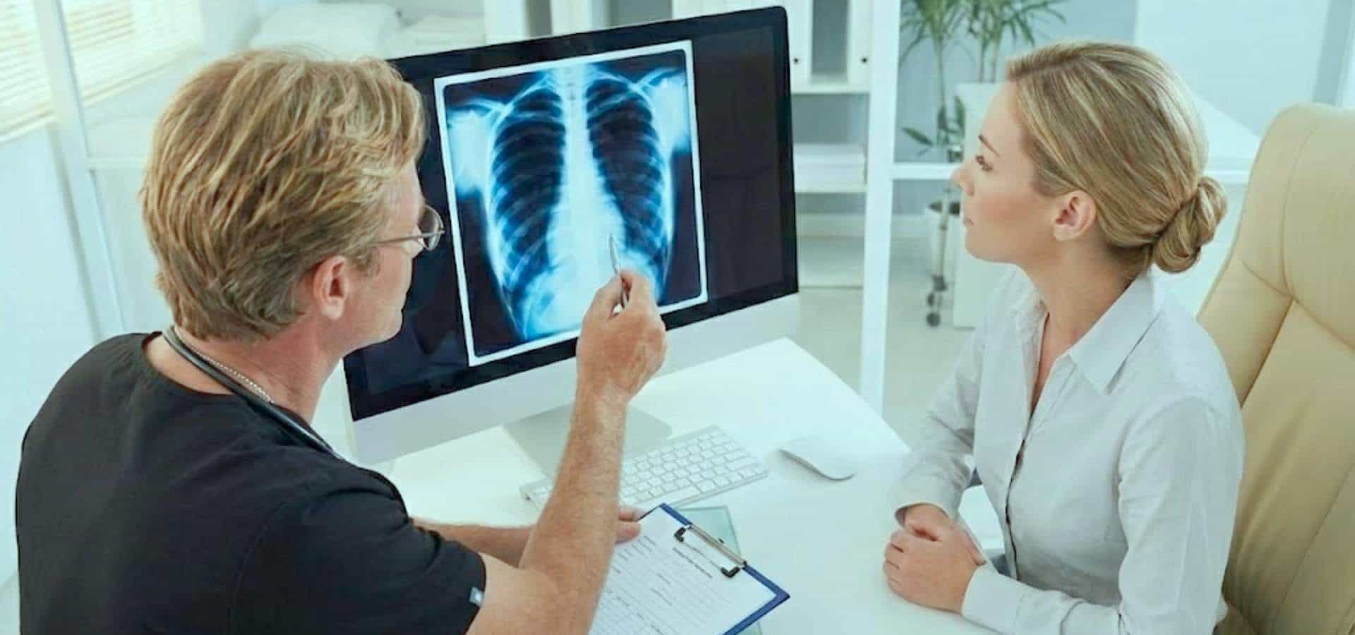 Doctor reviewing a chest X-ray on a computer screen and explaining the results to a female patient during a consultation in a modern medical office.