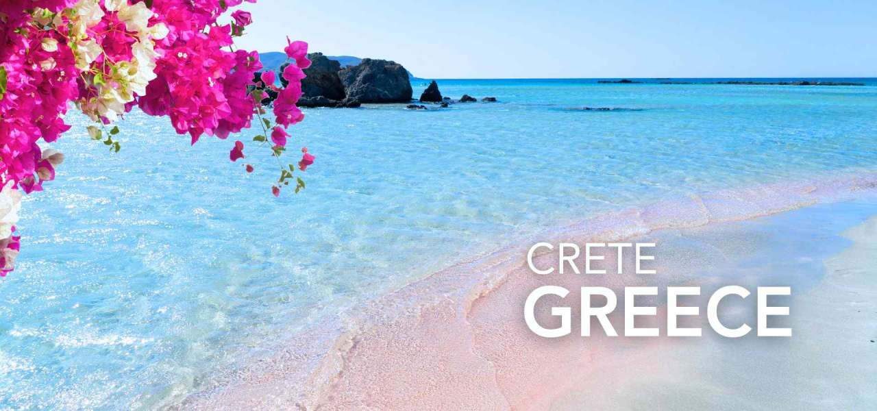 Beautiful beach in Crete, Greece, with crystal-clear turquoise water, soft pink sand, rocky coastline, and vibrant pink flowers overlooking the sea.