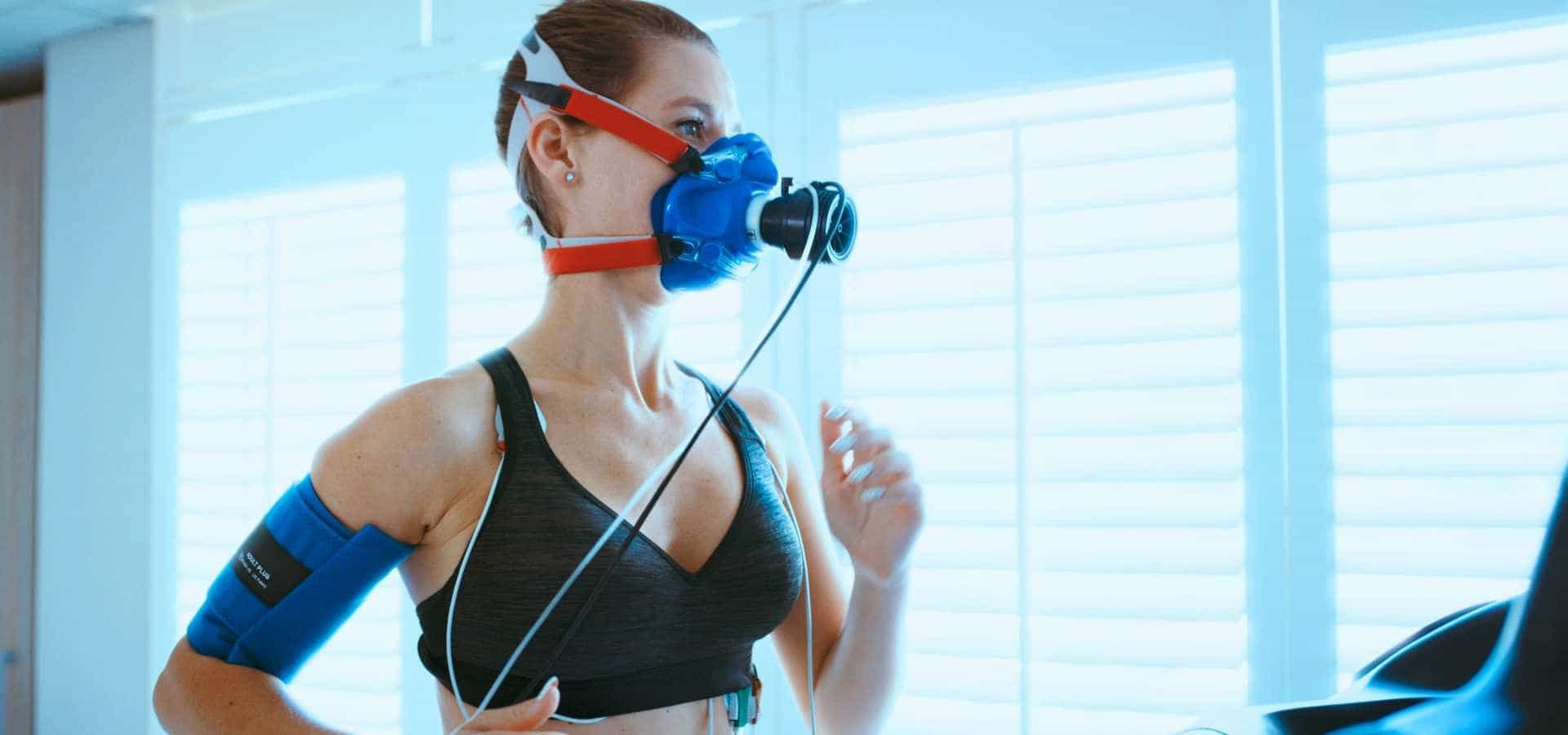 Woman running on a treadmill wearing a mask for VO2 max testing to measure fitness and oxygen use.
