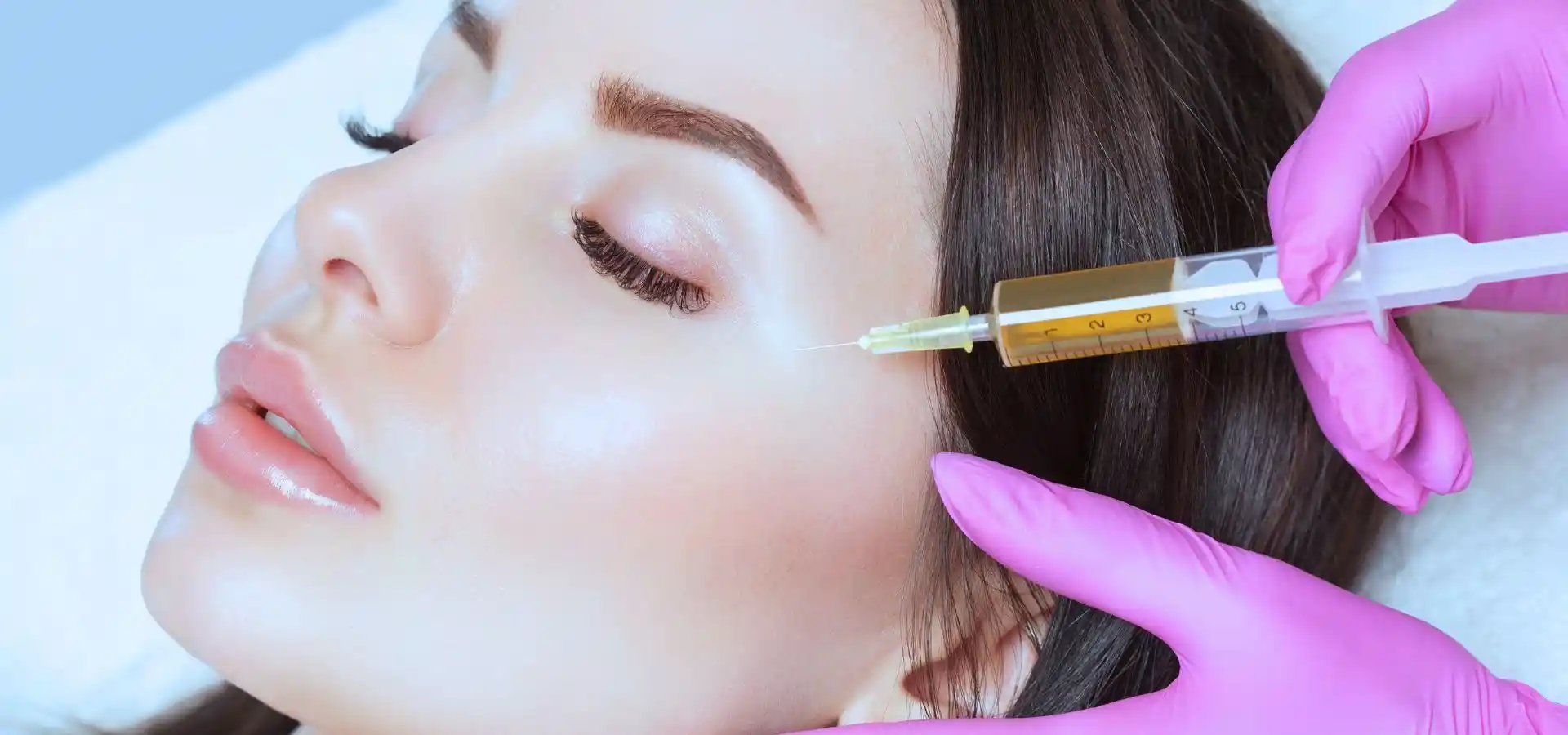 A close-up of a woman receiving a facial injection near her cheek from a professional wearing pink gloves, highlighting PRP or cosmetic therapy treatment.