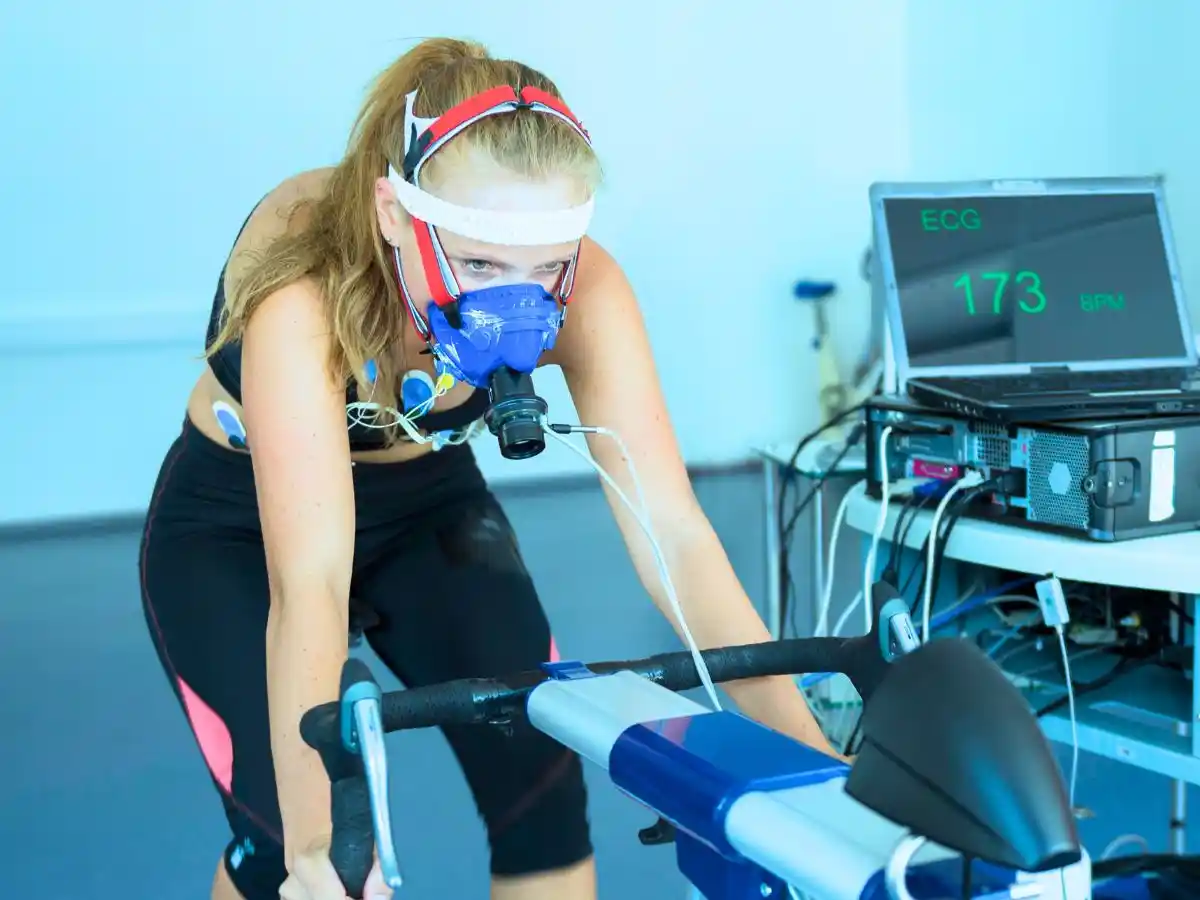 Woman undergoing a cardiopulmonary exercise test on a stationary bike with ECG monitoring.