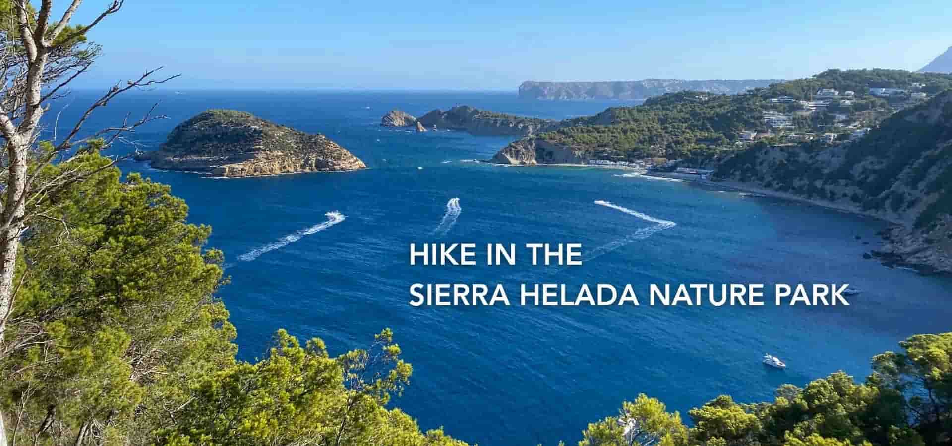 Panoramic coastal view of Sierra Helada Nature Park with blue sea, green hills, rocky islands, and boats moving across the water.