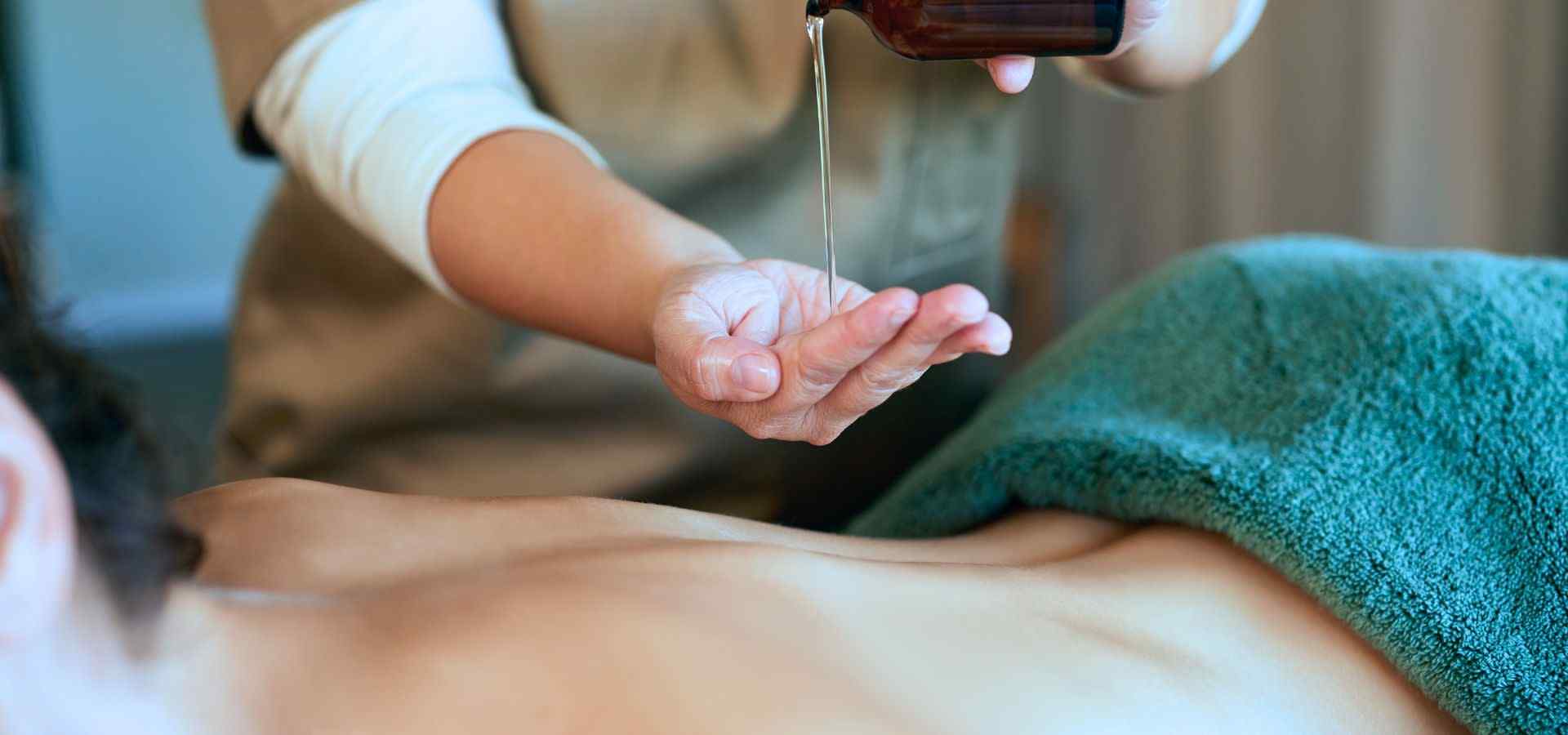 Close-up of an Ayurvedic wellness treatment, with a therapist gently pouring warm herbal oil onto a client’s back during a relaxing spa therapy session.