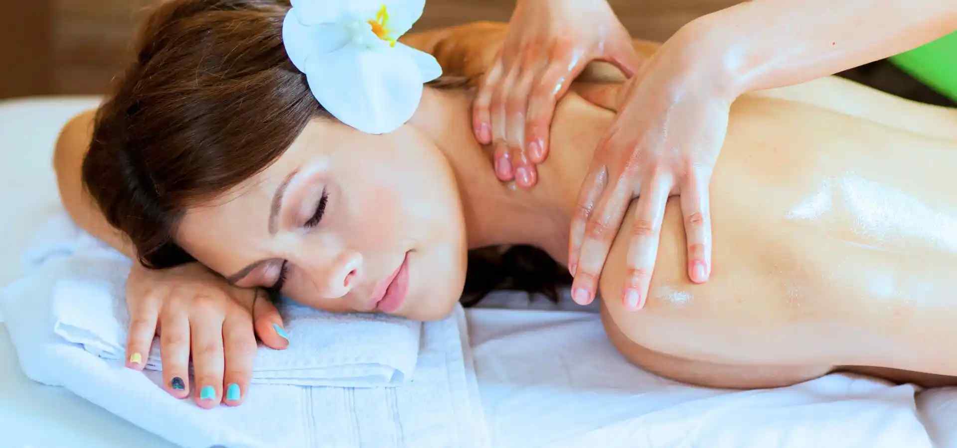 Woman enjoying a relaxing spa massage, lying comfortably on a treatment table while a therapist performs a soothing shoulder and back massage with aromatic oils in a wellness setting.