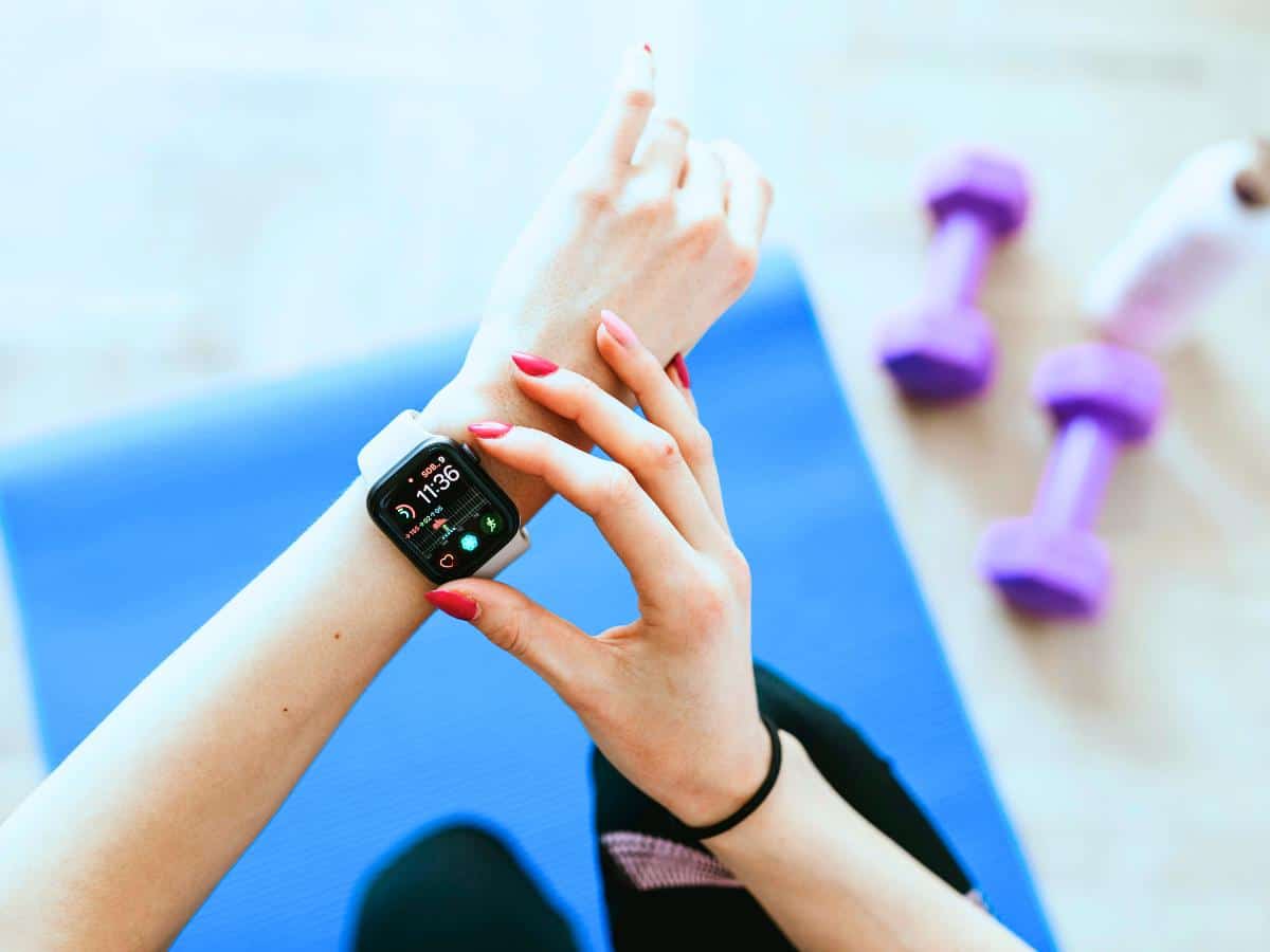 Close-up of a woman checking a smartwatch during a workout, with dumbbells and yoga mat in the background, showing fitness and health tracking.