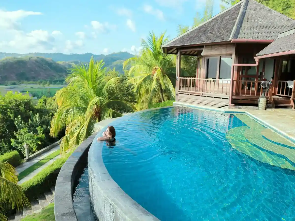 Luxury infinity pool overlooking tropical mountains and lush palm trees beside a modern villa.