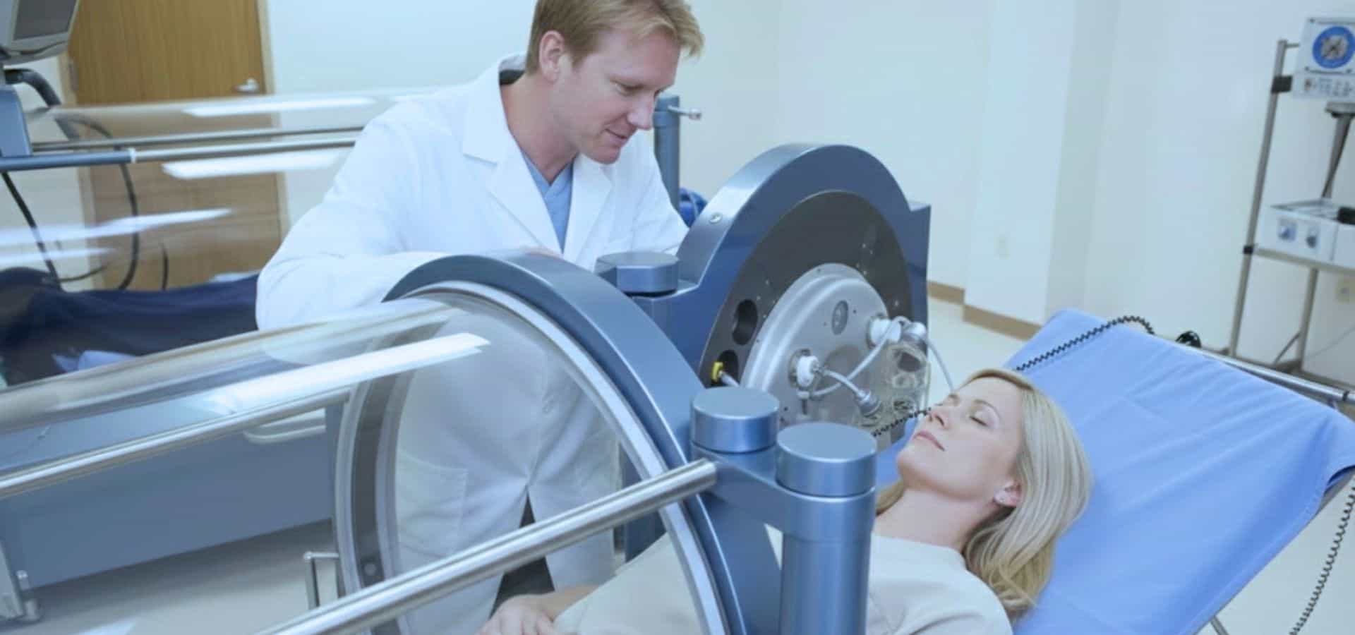 Doctor in a white coat assisting a female patient lying on a medical bed inside a cylindrical hyperbaric oxygen therapy chamber in a clinical setting.